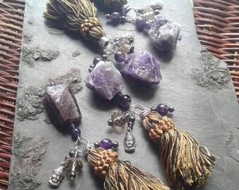 Può includere: Due paia di orecchini con cristalli di ametista, nappe dorate e verdi e ciondoli d'argento. I ciondoli includono una testa di Buddha e un piccolo cristallo.