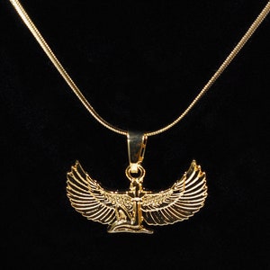 K&ouml;nnte beinhalten: Eine goldene Kettenkette mit einem Anh&auml;nger, der eine gefl&uuml;gelte Figur mit einem stilisierten Design zeigt. Der Anh&auml;nger ist ein Symbol der alten &auml;gyptischen Mythologie.