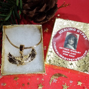K&ouml;nnte beinhalten: Goldkette mit gefl&uuml;geltem Anh&auml;nger in einer wei&szlig;en Schachtel. Die Schachtel befindet sich auf einem roten Hintergrund mit goldenen Sternen. Die Schachtel tr&auml;gt ein Etikett mit der Aufschrift "Healing Gypsy Artisan Jewelry Made Just For You! TheHealingGypsy@Etsy.com"