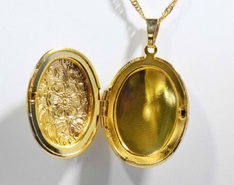 Könnte beinhalten: Goldene ovale Halskette mit Anhänger, der auf der Vorderseite ein Blumenmuster und im Inneren eine leere Fläche hat. Der Anhänger ist geöffnet und die Kette ist sichtbar.