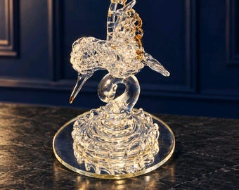 Figura de colibrí de vidrio hilado con detalles dorados sobre base espejada