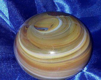 May include: A large, round, glass paperweight with swirling patterns of brown, yellow, and white. The paperweight has a crack on the surface.