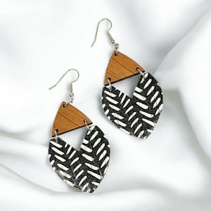 May include: A pair of black and white geometric patterned wooden earrings with a brown wood accent. The earrings have a teardrop shape and are suspended from silver hooks.