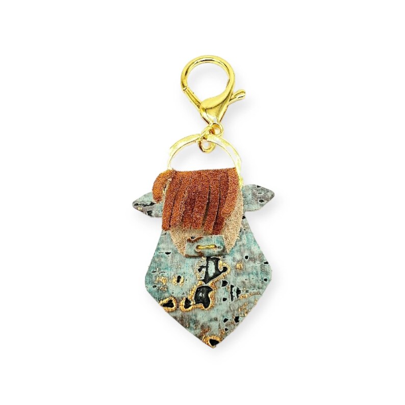 May include: A unique keychain featuring a turquoise and gold-toned pendant with a brown leather fringe and a gold-colored clasp. The pendant has a geometric shape and a distressed finish, adding a rustic charm.