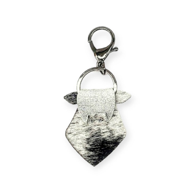 May include: Silver-toned keychain with a small, diamond-shaped bag charm. The bag has a flap with a small, round handle.