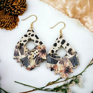 May include: A pair of dangle earrings with a geometric shape. The earrings are made of wood and feature a floral print with black and white accents.