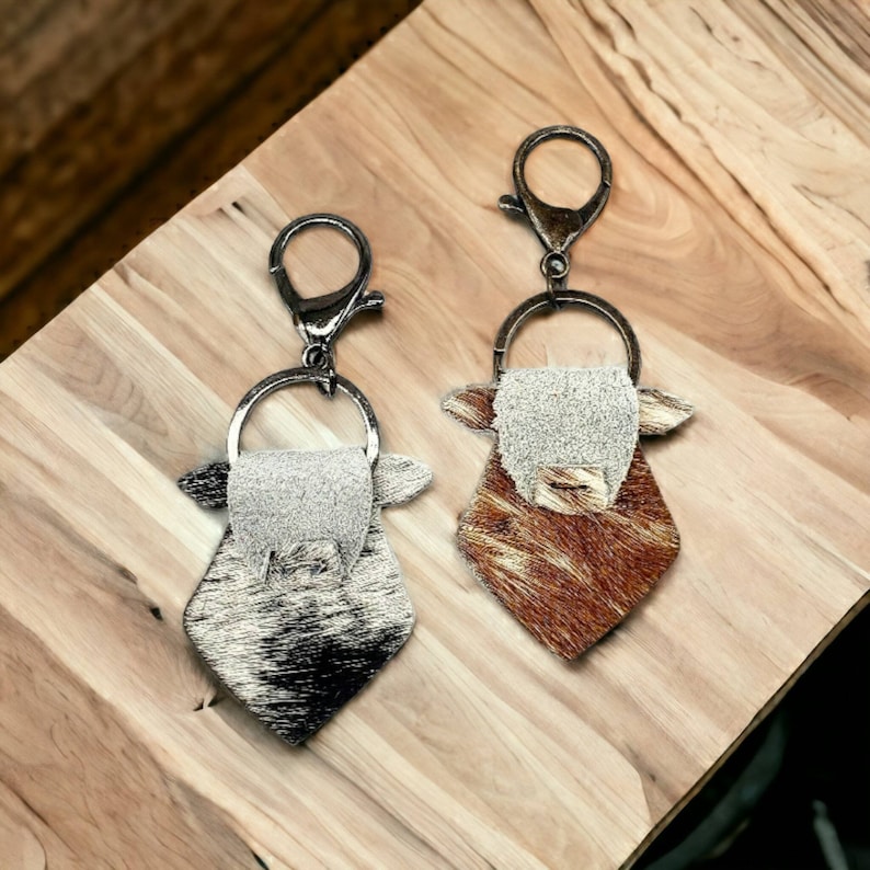 May include: Two cowhide keychains with silver key rings. One keychain is brown and white, the other is black and white.