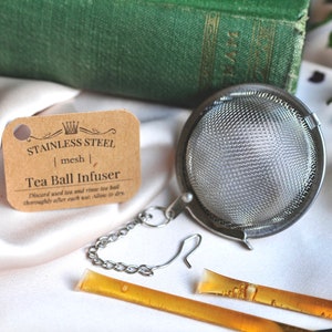 May include: A stainless steel tea ball infuser with a mesh design. The infuser is attached to a chain and has a hook for hanging. The label reads "Stainless Steel | mesh | Tea Ball Infuser".