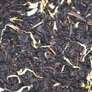 May include: Close-up of black tea leaves with dried orange and white flower petals.