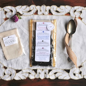 May include: A set of four loose leaf tea blends in a clear plastic bag with gold trim. The tea blends are labeled "Queen's Rose", "King's Favorite", "Queen's English", and "The Royal Lavender Earl Grey".
