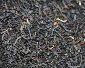 Könnte beinhalten: Nahaufnahme von schwarzen Teeblättern mit einer Mischung aus schwarzen und braunen Stücken. Die Teeblätter sind lose und bereit zum Aufbrühen.