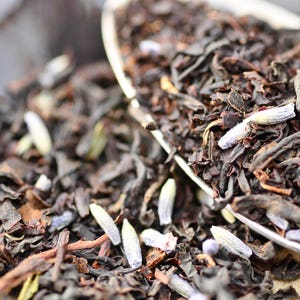 May include: Close-up of a mixture of black tea leaves and lavender buds. The tea leaves are dark brown and the lavender buds are light purple.