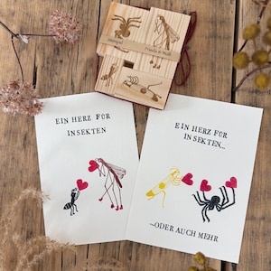 Può includere: Timbri in legno con disegni di insetti e i testi "Stempel" e "Frieda & Wolfi" sono mostrati con due biglietti. I biglietti presentano illustrazioni di insetti che tengono cuori, con il testo tedesco "EIN HERZ FOR INSEKTEN" e "...ODER AUCH MEHR".