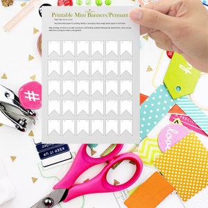 Può includere: Un foglio di mini banner/stendardi stampabili. Il foglio è tenuto in mano e circondato da materiali per l'artigianato, tra cui forbici rosa ed etichette colorate. Il testo "Printable Mini Banners/Pennant" è visibile.