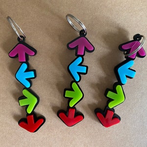 Puede incluir: Tres llaveros con una serie de flechas de colores. Las flechas son rojas, verdes, azules y rosas. Los llaveros están unidos a anillos plateados.