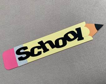 May include: A yellow paper pencil with the word "School" in black letters. The pencil has a pink eraser, a silver ferrule, and an orange and black tip. The pencil is a back-to-school themed craft.