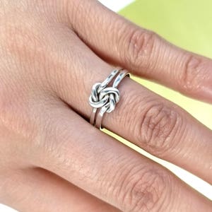 May include: A silver knot ring with a simple design. The ring is worn on a finger.