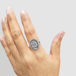May include: A silver ring with a black oval-shaped stone featuring a monogram of the letters "BFM".
