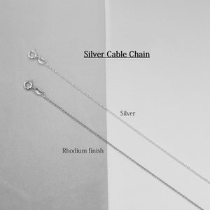 May include: Two silver cable chains, one with a rhodium finish. The chains are displayed on a white and gray background. Silver Cable Chain.