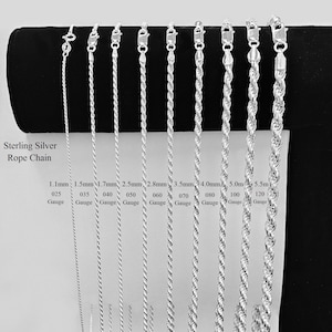 Op de afbeelding: Een collectie van negen sterling zilveren touwkettingen met verschillende diktes, variërend van 1,1 mm tot 5,5 mm. Elke ketting heeft een karabijnsluiting aan de bovenkant. Tekstlabels geven de specifieke breedte en dikte van elke zilveren ketting aan.