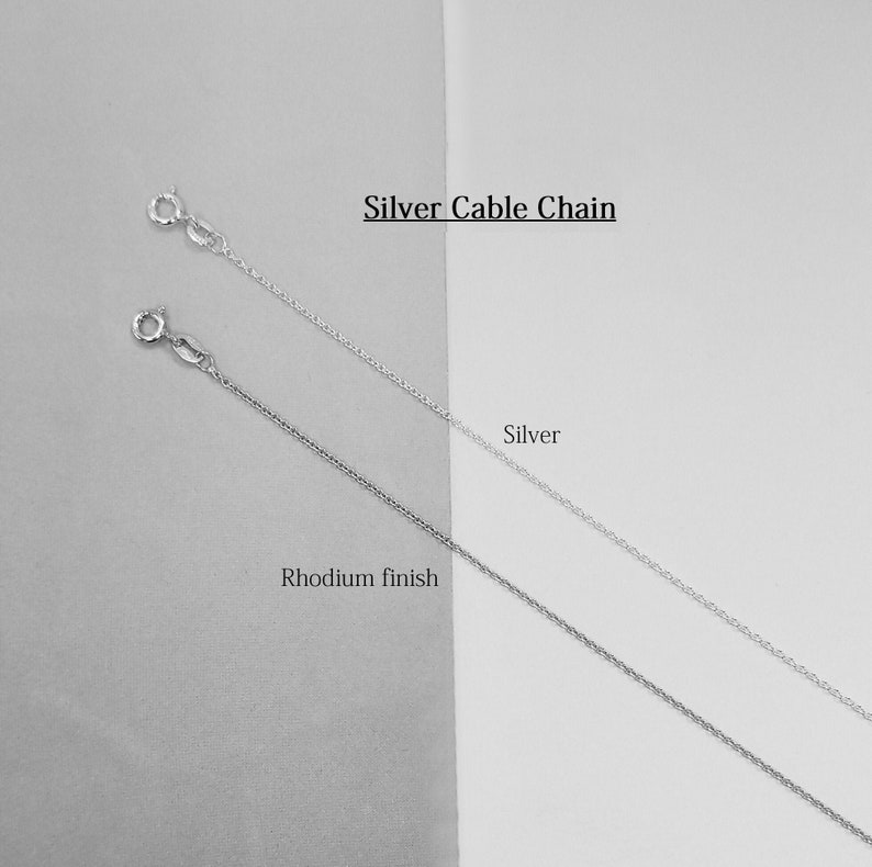 May include: Two silver cable chains, one with a rhodium finish. The chains are displayed on a white and gray background. Silver Cable Chain.