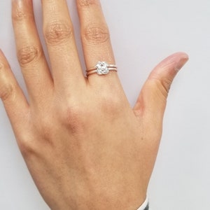 May include: A silver ring with a knot design. The ring is worn on the ring finger of a person's hand.
