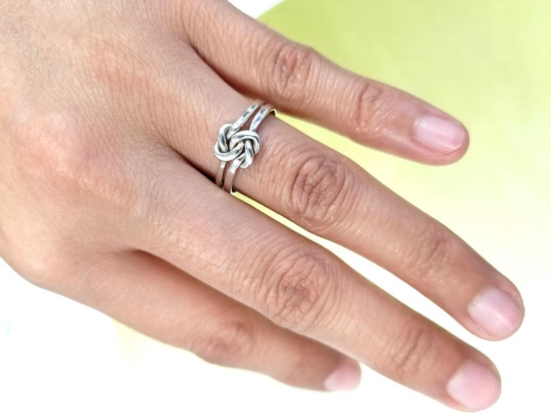 May include: A silver knot ring with a simple design. The ring is worn on a finger.