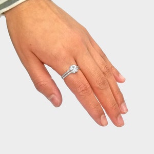 May include: A silver ring with a knot design. The ring is worn on the index finger of a hand.