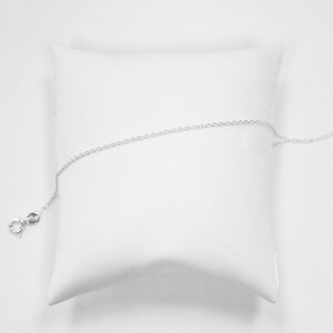May include: A silver chain necklace with a lobster clasp closure. The chain is displayed on a white pillow.