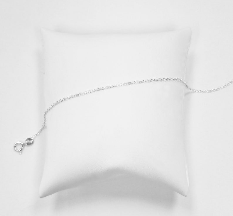 May include: A silver chain necklace with a lobster clasp closure. The chain is displayed on a white pillow.