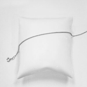May include: A silver chain necklace on a white pillow. The chain is delicate and has a simple design.