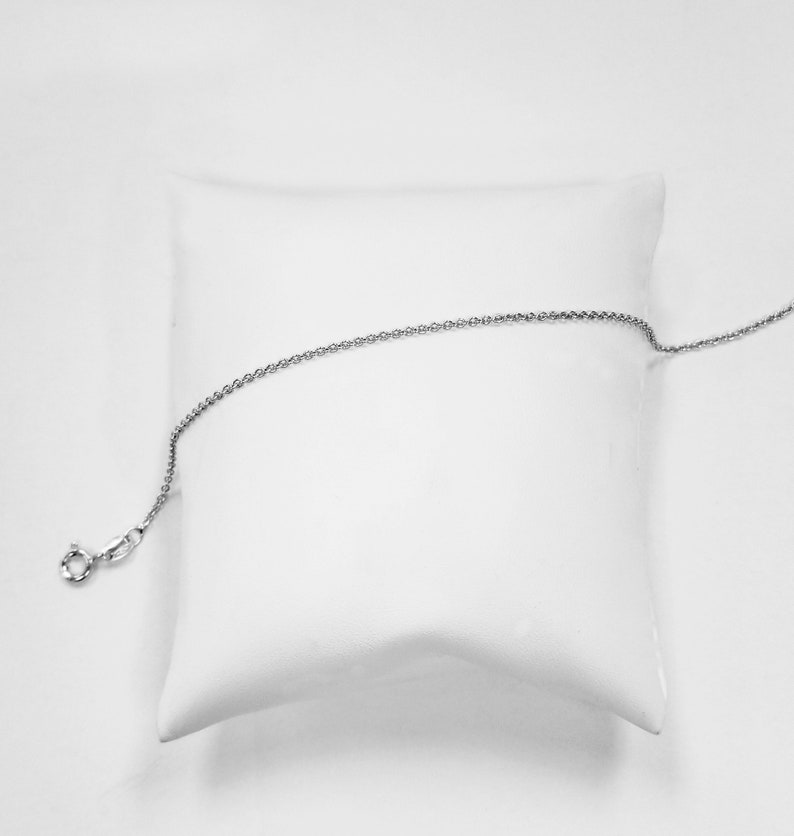 May include: A silver chain necklace on a white pillow. The chain is delicate and has a simple design.