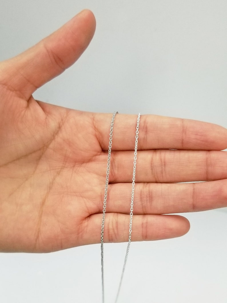 May include: Two silver chains of different lengths, laid out on a hand, showing the difference in length.