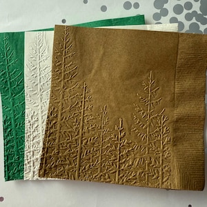 Könnte beinhalten: Drei Papierservietten mit einem geprägten Waldmotiv. Die Servietten sind grün, weiß und braun.