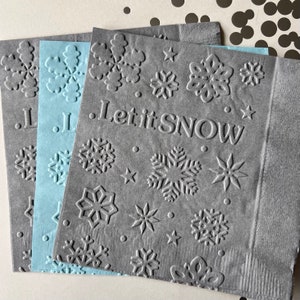 Puede incluir: Tres servilletas de papel grises con un dise&ntilde;o de copo de nieve y el texto "Let it Snow". Las servilletas est&aacute;n apiladas una encima de la otra.
