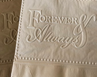 May include: Two square paper napkins, one cream and one tan, featuring an embossed border of small dots and the text Forever & Always in a combination of serif and script fonts. The napkins have a textured, creased surface and a ribbed bottom edge.