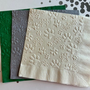 May include: Three paper napkins with an embossed paw print design. The napkins are green, grey, and white.