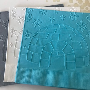 May include: Three paper napkins with an embossed design. The top napkin is blue with a white igloo design and white snowflakes. The middle napkin is white with white snowflakes. The bottom napkin is gray with white snowflakes.