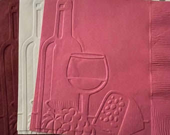 Puede incluir: Tres servilletas de papel rosas con un diseño en relieve de una botella de vino, una copa de vino y una cuña de queso. Las servilletas están dobladas en tres.