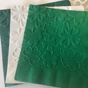 May include: Three green paper napkins with a raised shamrock design. The napkins are folded in thirds and stacked on top of each other.