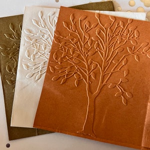 May include: Three embossed paper cards with a tree design. The cards are in shades of brown, white, and green.