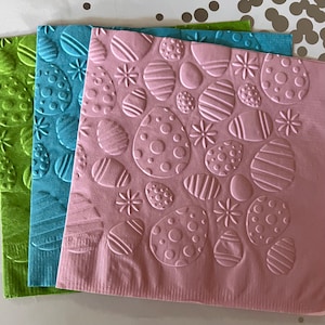 May include: Three pink, blue and green paper napkins with an embossed pattern of various shapes, including circles, ovals and flowers.