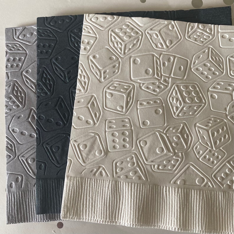 May include: Three paper napkins with an embossed dice pattern. The napkins are in shades of gray and white.