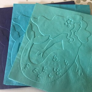May include: Three teal blue paper napkins with a raised embossed design of a mermaid with a star on her head. The mermaid's tail has scales and the text "See You" is embossed on the napkin.