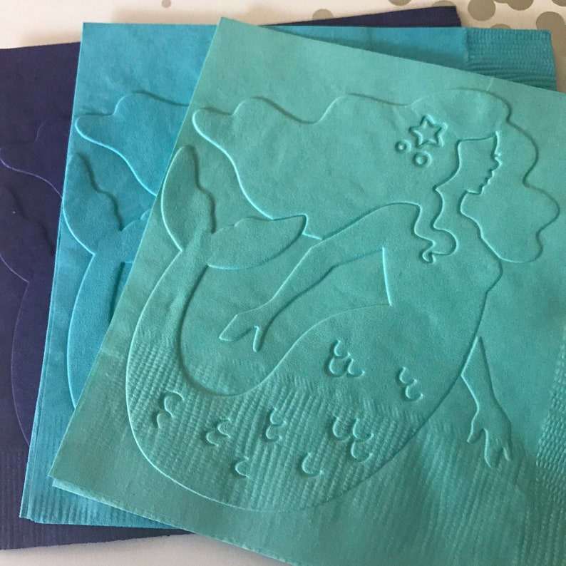 May include: Three teal blue paper napkins with a raised embossed design of a mermaid with a star on her head. The mermaid's tail has scales and the text "See You" is embossed on the napkin.