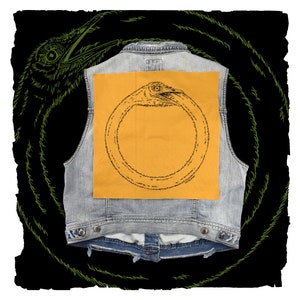 May include: A denim vest with a yellow patch featuring a black line drawing of a bird's head forming a circle.