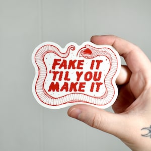Puede incluir: Pegatina blanca con un diseño de serpiente roja y el texto "Fake it til you make it".