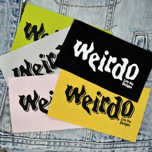 May include: A collection of rectangular patches in various colors, including black, yellow, pink, gray, and green. Each patch features the word "Weirdo" in a stylized font, with "Lofty Dog Designs" printed on some.