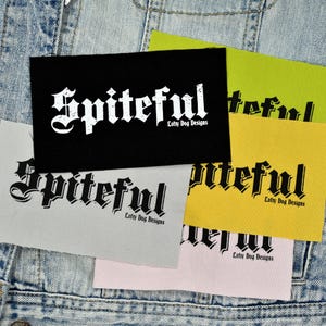 May include: Several fabric patches in different colours, including black, yellow, and light grey. Each patch displays the word "Spiteful" in a gothic font, with "Lofty Dog Designs" underneath. The patches are set against a denim background.