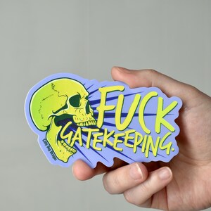 May include: A sticker with a yellow skull graphic and the words "FUCK GATEKEEPING" in yellow on a blue background. The sticker has a unique shape and the text "Lolly Dog Designs" is visible.